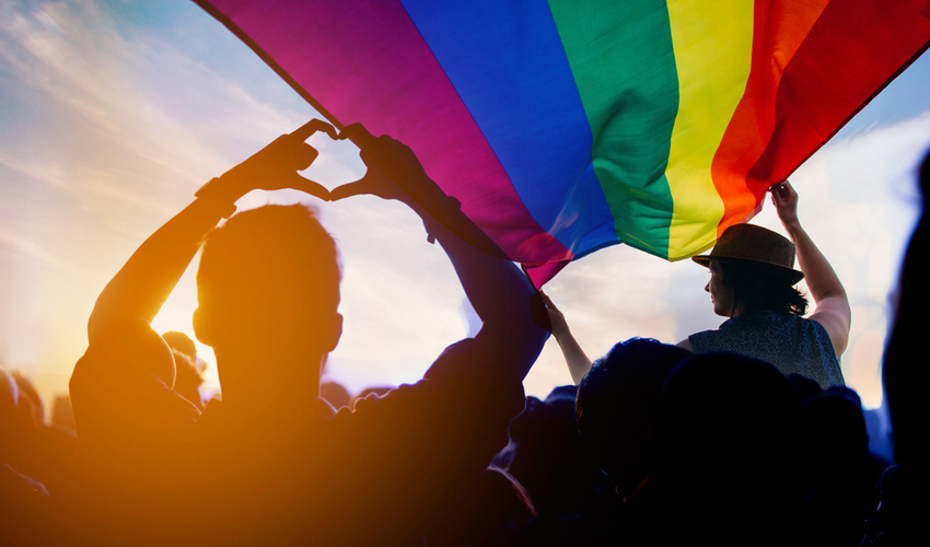 Pride community at a parade with hands raised and the LGBTQ flag