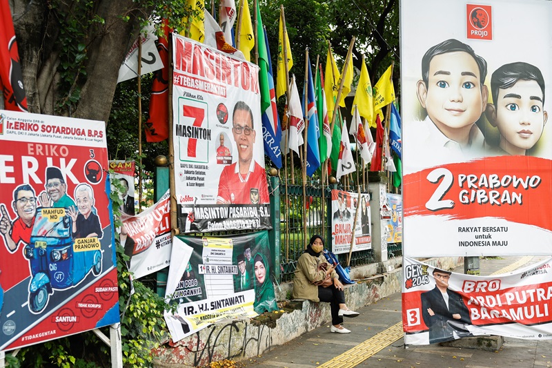 a woman sits near flags and posters promoting the presidential and legislative candidates ahead of general election in jakarta